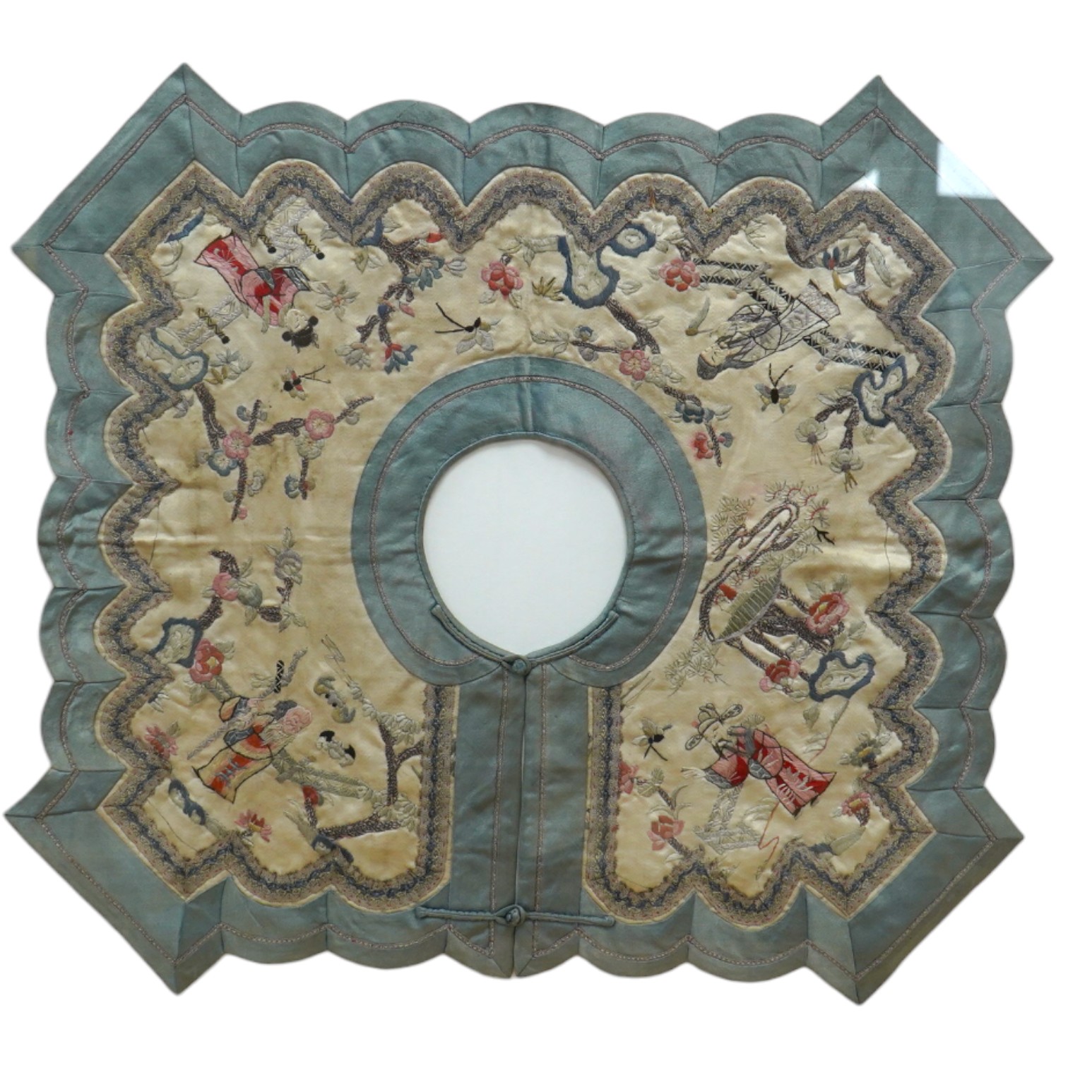 A framed Chinese ornate embroidered collar with scalloped edge, embroidered on cream silk, with polychrome silks, of figures, blossom, butterflies and auspicious symbols, the edges scalloped and braided with an outer blu